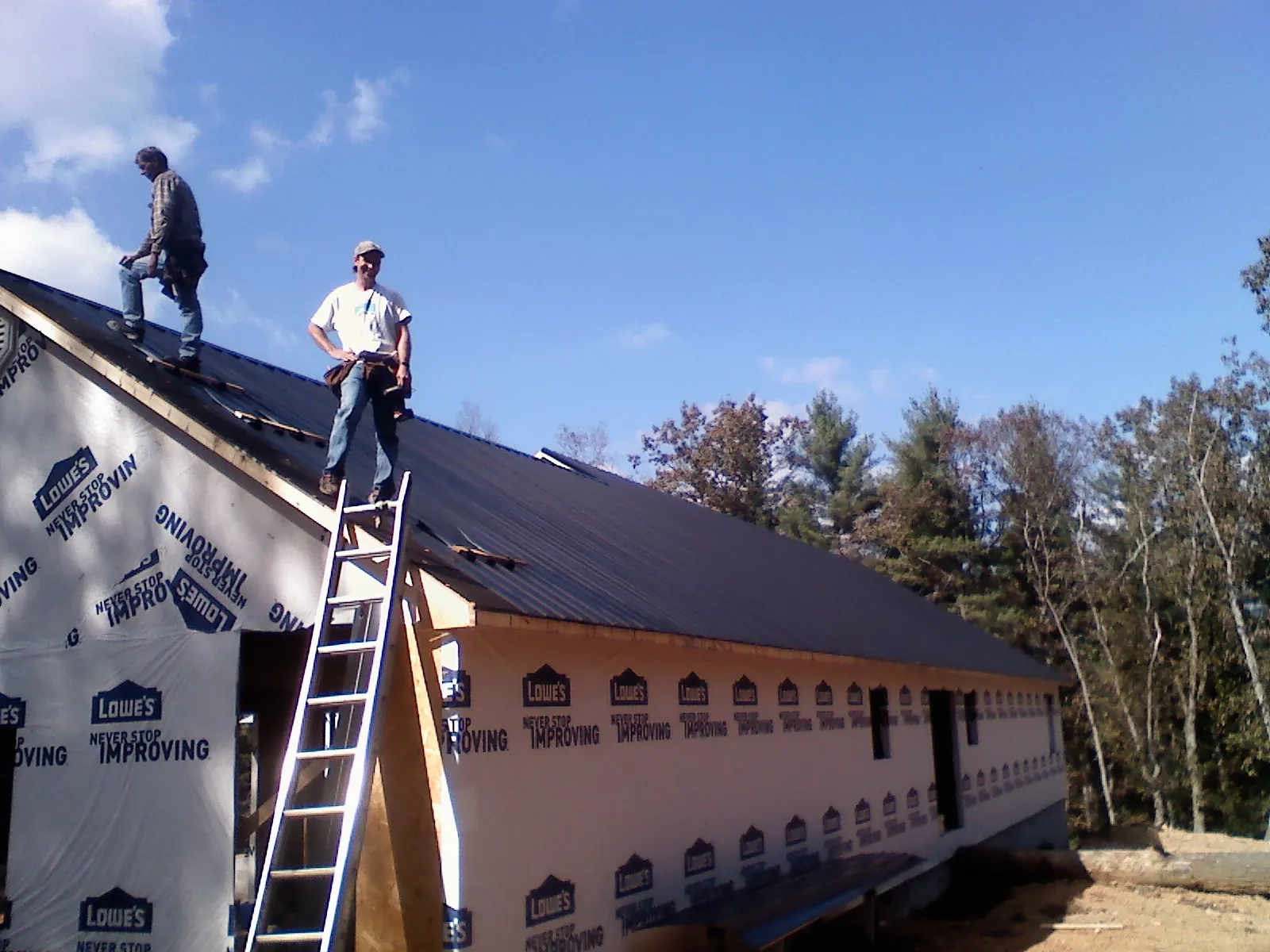 Two roofers standing on a long dark metal roof over a wrapped building in Highland